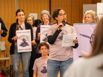 A community member speaks at the state capitol in support of public schools surrounded by team members holding signs in support.