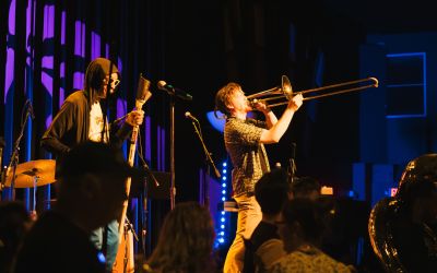 Musicians play instruments on stage in front of a silhouetted audience in support of MN United Performers.