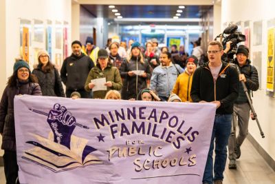 Community members march inside the Minneapolis Public Schools' Davis Center building behind a banner that reads "Minneapolis Families for Public Schools".