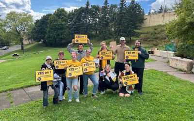 A team of people standing in a a grassy lawn, holding yellow "Yes on 1" campaign signs