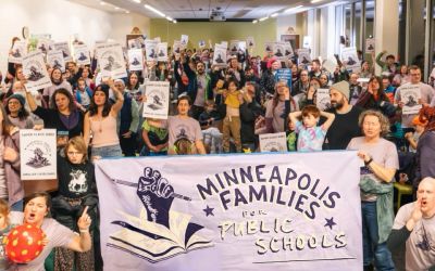 A large crowd of people gathered behind a Minneapolis Families for Public Schools banner, some holding up signs.