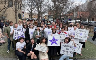 A group of people standing outside a venue, holding signs in support of Twin Cities United Performers