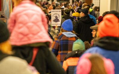 view from behind of a large group of community members marching together holding signs supporting education.