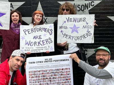 Members of Twin Cities United Performers stand in front of the iconic star wall at First Avenue nightclub with signs supporting the work of performers.