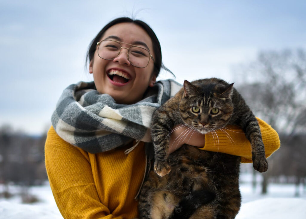 LyLy Vang-Yang holds her cat Bella up and laughs at the camera. Behind them is the blue sky and