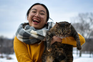 LyLy Vang-Yang holds her cat Bella up and laughs at the camera. Behind them is the blue sky and