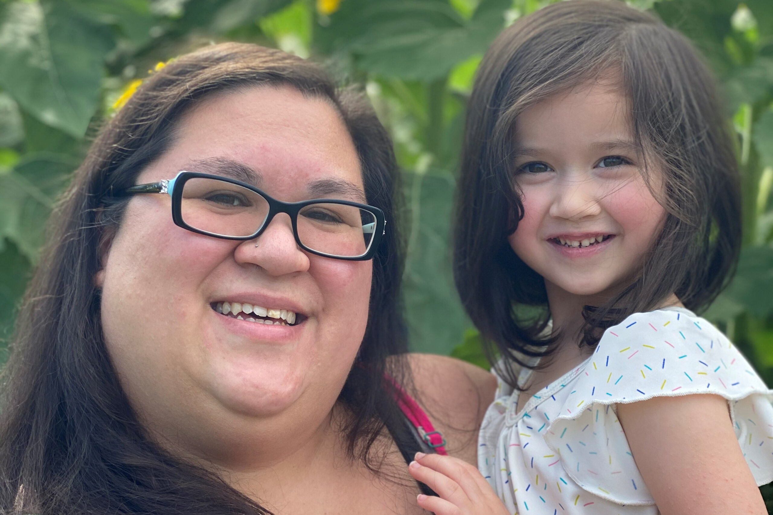 A photograph of TakeAction leader Megan holding her daughter Imogene, with greenery in the background.