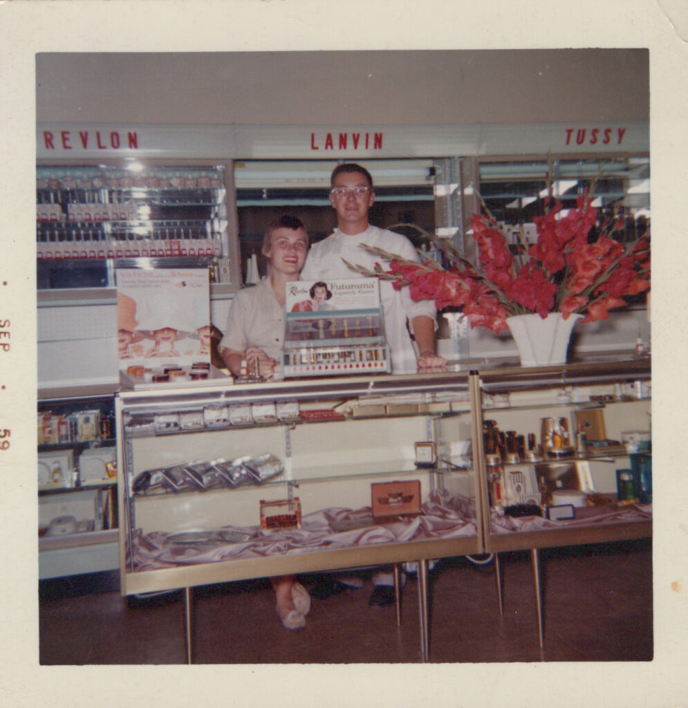 A 1959 photograph of Laura's grandparents, Mary Aspenes (left) and Donald Aspenes at College Pharmacy. The couple smiles at the camera from behind the cosmetics display. 