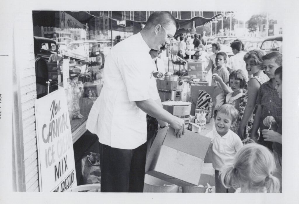 A black and white photograph of Laura's grandpa, Donald Aspenes, handing out treats the local children outside his pharmacy. 