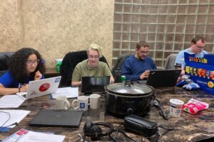 Photo of four people seated around a table, working on laptops and phones.