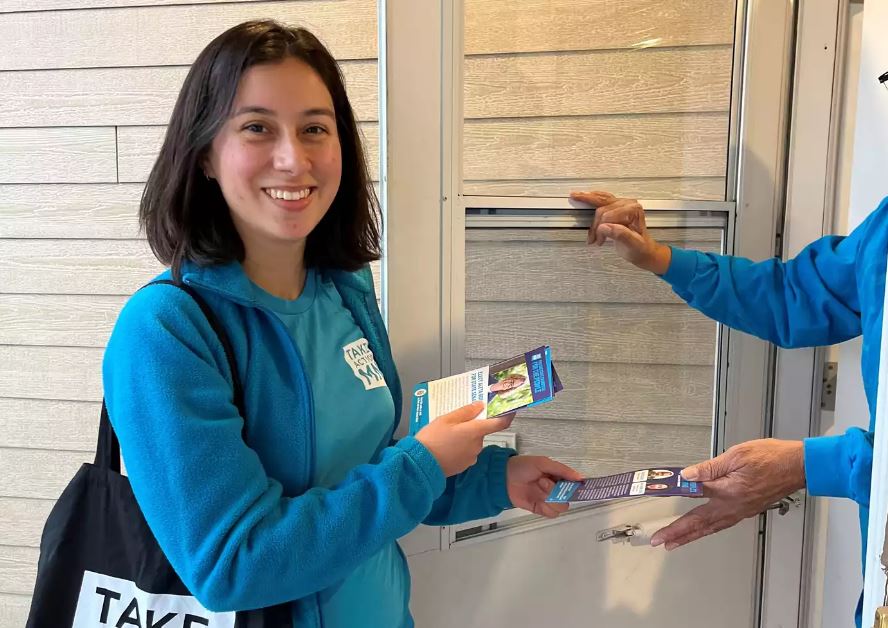 A woman in a blue shirt handing pamphlets to a person at a door